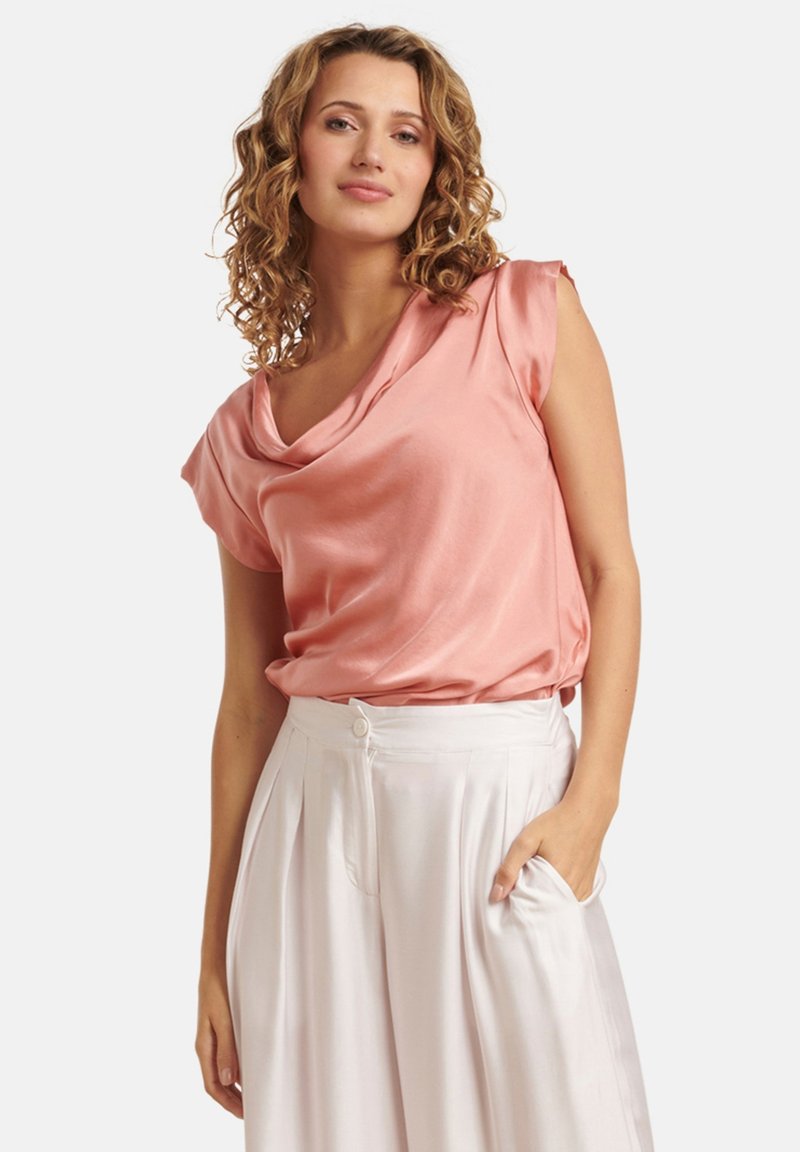 Roze satijnen blouse met een gedrapeerde halslijn, korte mouwen, gecombineerd met lichtgekleurde, high-waisted plissébroeken.