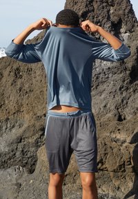 Tenue de sport comprenant une chemise à manches longues bleue et un short gris. La chemise est lisse avec une coupe décontractée, et le short possède des poches latérales.