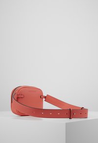 Borsa a tracolla rossa in pelle con chiusura a zip, forma arrotondata, tracolla piatta con fori per la regolazione e logo embossato sul davanti.
