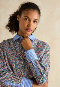 Floral shirt with a blue striped collar and cuffs. Features multicolored floral pattern on a white background, button-down front, and long sleeves.