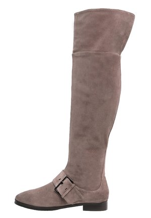 Botte en daim taupe montant au-dessus du genou avec un petit talon bloc et une large sangle avec une boucle noire près de la cheville.