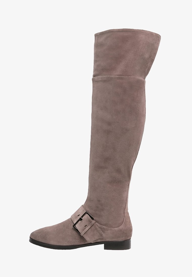 Botte en daim taupe montant au-dessus du genou avec un petit talon bloc et une large sangle avec une boucle noire près de la cheville.