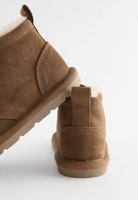 Braune Wildleder-Ankle-Boots mit weichem Fellfutter, strukturiertem Gummisohle und einem Stoffzugband an der Rückseite für ein einfaches An- und Ausziehen.