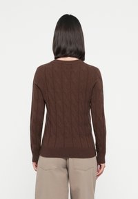 Brown knitted sweater featuring a textured cable pattern, ribbed cuffs, and hem; paired with light beige wide-leg trousers.