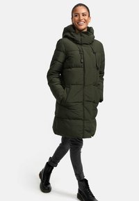 Long green puffer coat with a hood, featuring a front zipper, drawstrings, and side pockets. Paired with gray jeans and black ankle boots.