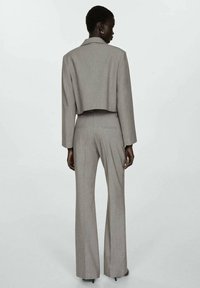 Blazer grigio tagliato con colletto a pistagna e pantaloni a gamba larga abbinati, caratterizzati da una texture liscia e linee pulite.