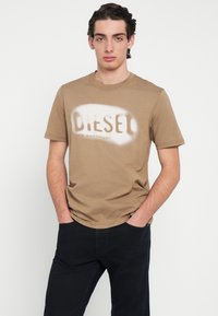 Μπεζ βαμβακερό T-shirt με ξεθωριασμένο λευκό λογότυπο "DIESEL" στο μέτωπο. Κοντά μανίκια και στρογγυλή λαιμόκοψη. Κανονική εφαρμογή.