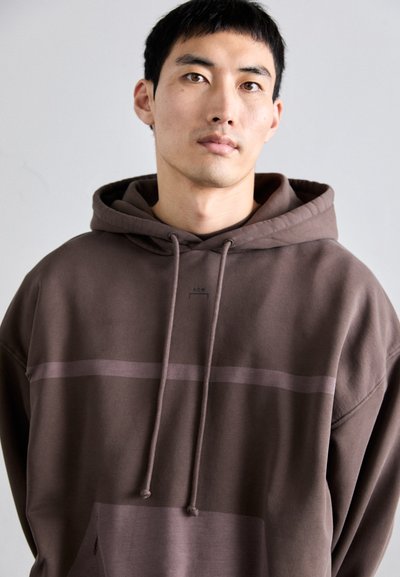 Sudadera marrón con cordón, con una raya horizontal en el pecho. Confeccionada en material suave y con un corte holgado.