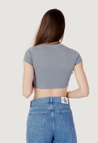 Top corto a righe grigio con maniche corte, abbinato a jeans in denim azzurri a vita alta con tasche posteriori e un'etichetta sulla vita.