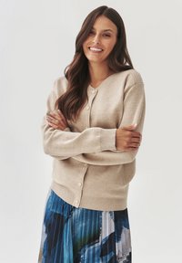 Beige cardigan met een ronde halslijn, geribbelde accenten en knoopsluiting. Gecombineerd met een geplooide, kleurrijk patroonrok.