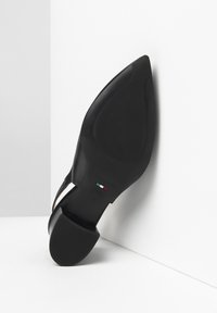 Chaussure à talon haut noire avec un bout pointu et un dessus en cuir texturé, présentant une semelle lisse et un accent aux couleurs du drapeau italien sur le talon.