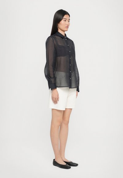 Sheer navy blue button-up shirt with vertical stripes, paired with white shorts and black flats. The shirt features a collar and long sleeves.