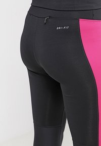 Mustat urheilulegginsit, joissa on vaaleanpunainen sivupaneeli, joustavaa kangasta, pienen vetoketjullisen taskun ja "DRI-FIT" -logon kanssa vyötäröllä.