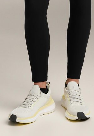 Chaussures de sport légères en gris et blanc, dotées d'une tige en mesh, d'accents jaunes et d'une semelle en caoutchouc à finition texturée.