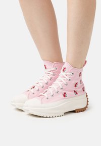 Vaaleanpunaiset korkeat kangastennarit, joissa on kukka-embroidointi, paksut valkoiset kumipohjat ja sahalaitainen ruskea ulkopohja. Nauhat kulkevat hopeisten rei'itysten läpi.