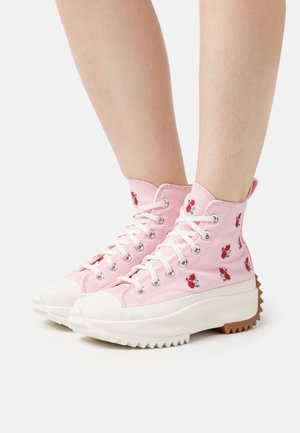 Růžové vysoké plátěné tenisky s květinovou výšivkou, silnými bílými gumovými podrážkami a zubatou hnědou podrážkou. Šňůrky provlečené stříbrnými očky.
