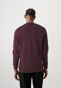 Sudadera burdeos de mezcla de algodón, con mangas largas y cuello redondo. Textura suave con puños y dobladillo acanalados.