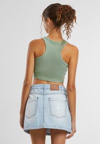 Un débardeur vert à côtes associé à une mini-jupe en denim bleu clair avec des poches arrière et une patch en cuir marron à la taille.