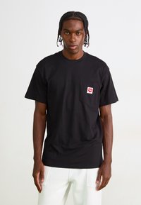 Black cotton t-shirt with a crew neck, short sleeves, and a red heart-shaped logo on the left chest pocket. Smooth texture.