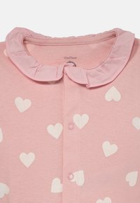 Une combinaison bébé rose avec des motifs de cœurs blancs, un col volé et une fermeture à boutons-pression, taille 12 mois/74 cm.