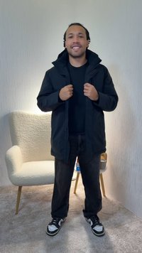 Melna rāvējslēdzēja jaka ar augstu apkakli, vilkta virs melnas krekla, kopā ar melnām biksēm un melnām un baltām sporta kurpēm. Gaišs fons.