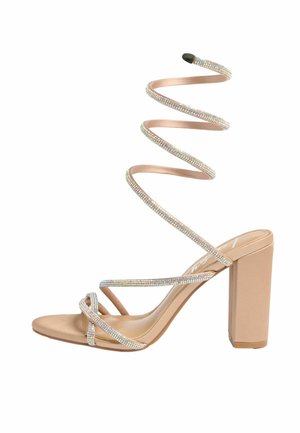 Bézs magas sarkú szandál blokk sarokkal és csavart strasszos pántokkal, amelyek a bokát körbetekercselik.