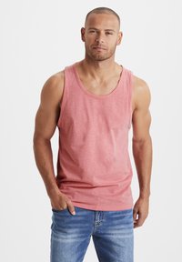 Red heathered tank top with a round neckline and slightly loose fit, paired with blue jeans. Fabric appears soft with a casual design.