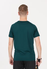 Mörkgrön idrottströja med korta ärmar och rund halsringning, tillverkad av ett slätt och lätt material. Har platta sömmar och en design på baksidan.