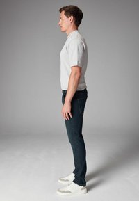 Polo shirt gris claro, jeans oscuros de corte slim, zapatillas blancas. Diseño minimalista con mangas cortas y textura sutil. Vista de perfil.