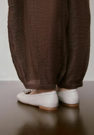 Balti odiniai batai be kulno, su plokščia pada ir subtiliais siuvimo detalėmis. Derinami su laisvais, rudais permatomais kelnėmis. Lygus paviršius, paprastas dizainas.