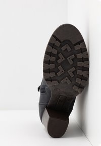 Suela de goma negra con un diseño texturizado, combinada con parte superior de cuero azul marino que presenta un hebilla lateral y detalles de costura.
