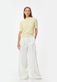 Lichtgele gebreide trui met korte mouwen en een opstaande kraag, gecombineerd met witte wijde broek met plooien en een gladde textuur.
