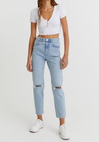 Vaqueros de cintura alta en un suave tono azul claro, con desgastes en las rodillas y corte recto, combinados con un top blanco corto de manga corta y zapatillas blancas.