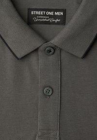 Polo gris pour homme avec bordure noire sur le col, deux boutons noirs et étiquette indiquant "STREET ONE MEN Expérience d'un confort inégalé."