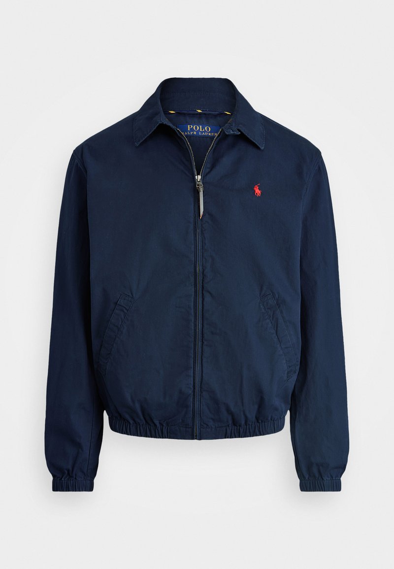 Donkerblauwe jacket van lichtgewicht stof, met een voorrits, elastische manchetten en zijzakken. Klein rood logo op de borst.