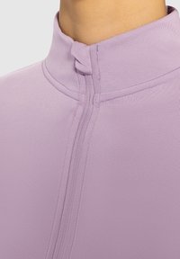 Lys lilla zip-up trøje med høj krave og synlige sømdetaljer. Glat, strækbart materiale designet til komfort og let bevægelse.