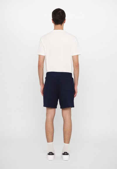 Calções azul-marinho feitos de tecido suave, com uma cintura plana e um único bolso traseiro, combinados com uma t-shirt branca simples.