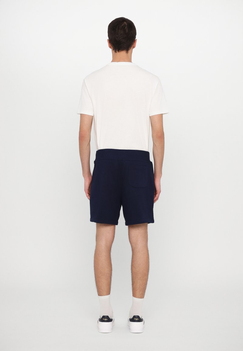 Shorts bleu marine en tissu doux, dotés d'une taille plate et d'une poche arrière unique, associés à un t-shirt blanc simple.