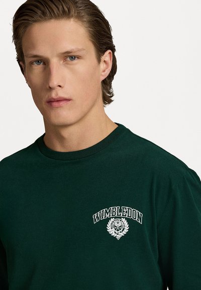 Donkergroen langemouwen t-shirt van katoen, met een witte 'Wimbledon' logo en een lauriertak ontwerp op de borst. Ronde hals.