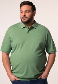 Zielona koszulka polo wykonana z miękkiego materiału, z kołnierzykiem, trzema guzikami i haftowanym logo na piersi. Krótkie rękawy i luźny krój.