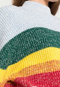 Pull en tricot avec un col montant, orné de rayures horizontales bleues, vertes, jaunes et rouges. Tissu texturé avec un aspect de fil mélangé.