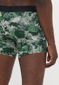 Zelena in siva boksarica z cvetličnim vzorcem, izdelana iz mehkega elastičnega materiala z črnim pasom.