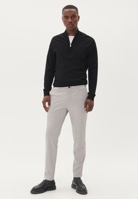 Fekete, cipzáras pulóver hosszú ujjal, világosszürke nadrággal párosítva. A lábbeli sötét, textúrázott felülettel rendelkezik. Egyszerű, modern dizájn.