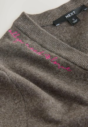 Grauer Pullover mit geripptem Kragen und pink gesticktem Text "all you need is love" auf der linken Seite. Weiche Textur und lässiges Design.