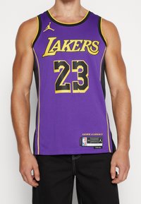 Violetti koripallopaita, jossa on keltaisia ja mustia yksityiskohtia. Sisältää tekstin "LAKERS" ja numeron "23" lihavoinnissa. Mukana hintalaput ja tekstuuri yksityiskohtia.