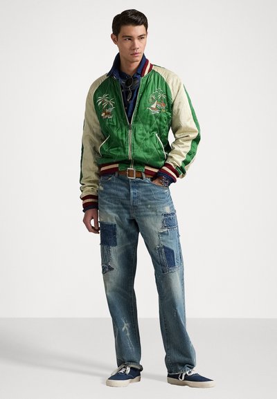 Grön och krämfärgad bomberjacka med broderade palmträd, kombinerad med slitna blåjeans med olika tyglappar och en avslappnad passform.