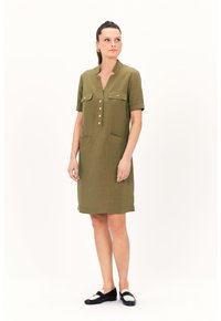 Abito in lino verde oliva con maniche corte, scollatura a V, chiusura frontale con bottoni, due tasche sul petto e una vestibilità rilassata.