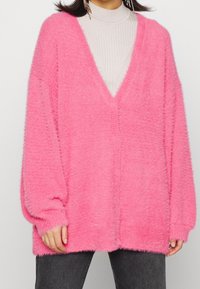 Fluffy pink oversized sweater with a deep V-neck, long sleeves, and ribbed texture. Soft material contrasts with the smooth inner layer.