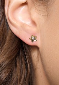 Złote kolczyki w kształcie kwiatu z małym kryształowym środkiem, przymocowane do małżowiny usznej, o gładkim wykończeniu i polerowanej fakturze.
