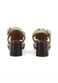 Sandali alti marroni con tacco largo a blocco, aperti sul retro e con cinturino alla caviglia regolabile. La parte superiore presenta un accento beige chiaro.